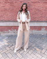 Woman in a neutral tailored suit with wide-led pants and Luna Selene nude heels, standing confidently against a brick wall.