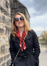 Woman wearing sunglasses, a black trench coat, and red Luna Selene silk scarf tied around her neck. 