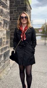 Woman wearing sunglasses, a black trench coat, and red Luna Selene silk scarf tied around her neck. 